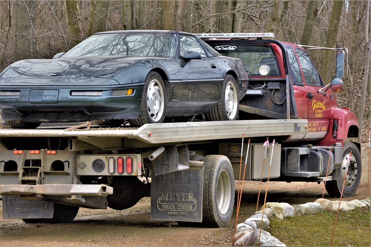 corvette, broken, needs repair, on truck, vehicle, transport, nature, automobile, sports car, hauled, remote, woods, forest, boondocks, large, wide, tires, powerful, fast car, going to repair shop, truck hauler, flatbed, flatbed hauler, brown car, brown shop, brown truck, brown power